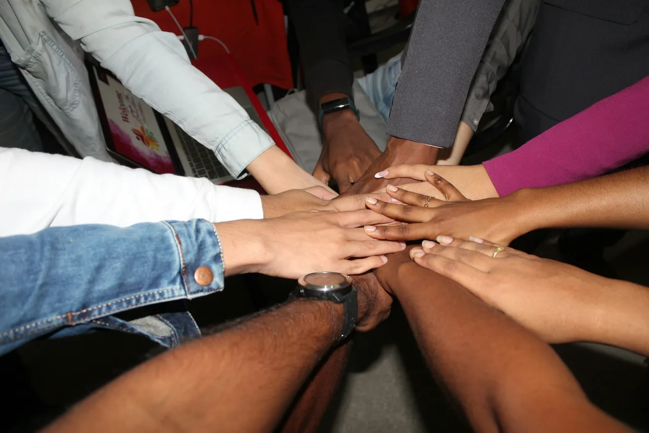 The hands of a team of people of different skin tones stacked together in the centre